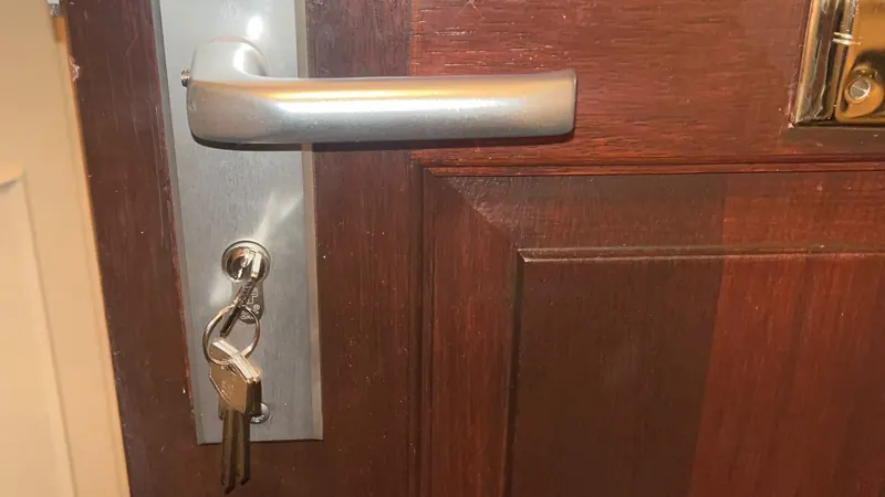 Buitengesloten / deur openen Sleutelbos in de cilinder aan de binnenkant van een houten voordeur, onder een aluminium deurkruk