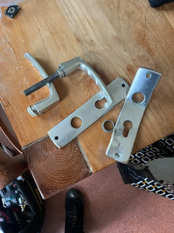 Hang- en sluitwerk vervangen Gedemonteerd oud deurbeslag: twee deurkrukken en twee langschilden op een houten tafel