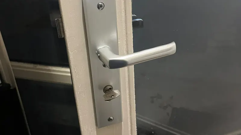 Hang- en sluitwerk vervangen Aluminium langschild met deurkruk en sleutel in de cilinder op een deur met glas