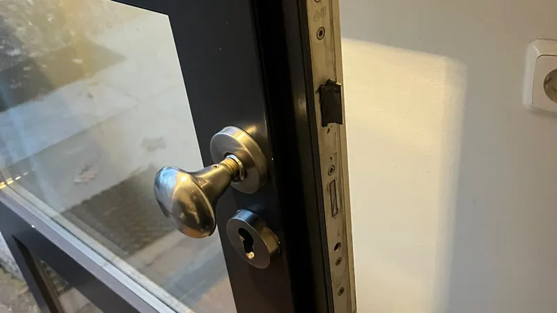 Hang- en sluitwerk vervangen RVS deurknop en cilinderrozet op een zwarte stalen deur met glas, voorplaat van het slot in de deurkant