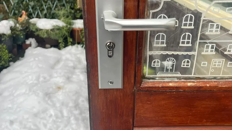 Hang- en sluitwerk vervangen Aluminium langschild met deurkruk en cilinder op een houten tuindeur, sneeuw op de achtergrond