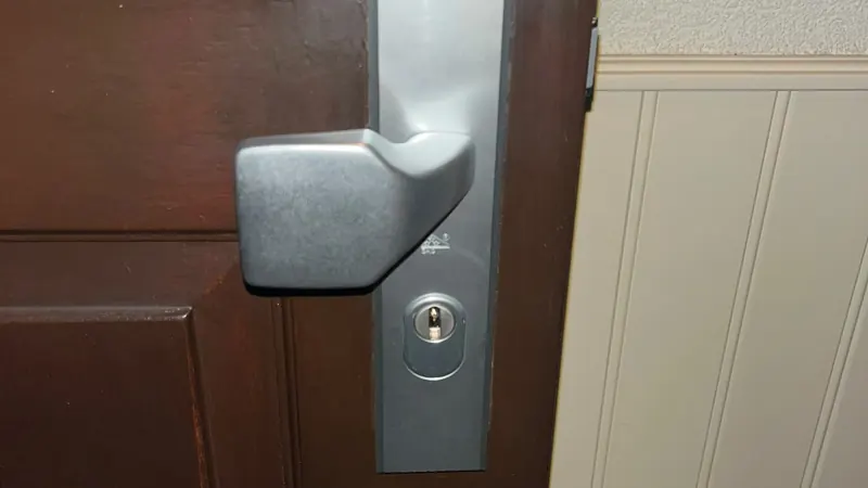 Aluminium veiligheidsbeslag met vaste knop en afgeschermde cilinder op een donkerbruine houten deur