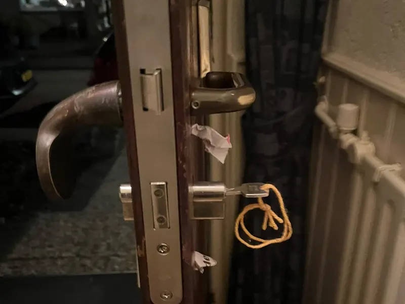 Insteekslot met voorplaat en cilinder in een geopende voordeur, sleutel aan een touwtje in het slot